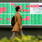 Pedestrians walk in front of a stock quotation board displaying the Nikkei share average and the yen-dollar conversion rate outside a brokerage in Tokyo