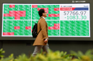 Pedestrians walk in front of a stock quotation board displaying the Nikkei share average and the yen-dollar conversion rate outside a brokerage in Tokyo
